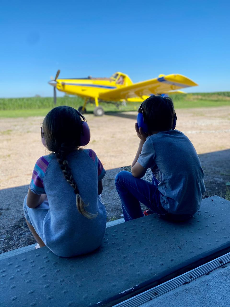 Two children in ear protection watching a crop duster on the runway